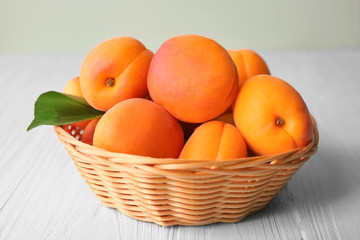 Wicker basket with fresh apricots on wooden table