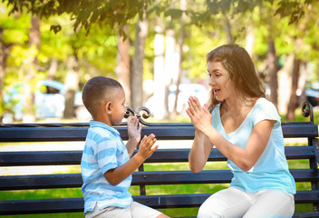 Young woman playing with adopted African American boy while sitting on bench in park