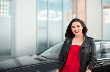 Beautiful overweight woman in red pantsuit standing near car on city street