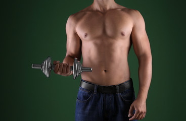Fototapeta na wymiar Sporty young man with dumbbell on dark color background