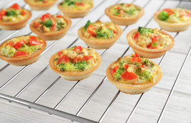 Baking grid with broccoli quiche tartlets on table