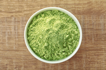 Bowl with wheat grass powder on wooden table