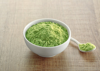 Bowl and spoon with wheat grass powder on wooden table