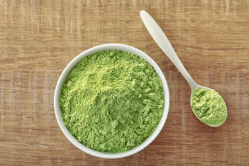 Bowl and spoon with wheat grass powder on wooden table