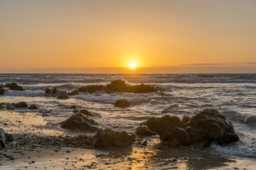 sunrise on a beach with waves and stones in the water