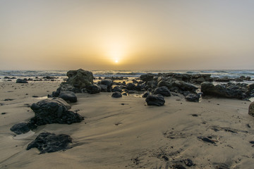 sunrise on a beach with waves and stones in the water