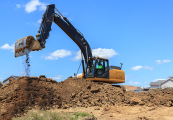 Backhoe on mound of dirt excavating a job site. 