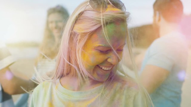 Close-up Portrait of a Beautiful Blonde Girl Dances in Celebration of Holi Festival With Her Friends. Her Face and Clothes are Covered with Colorful Powder. Shot on RED EPIC-W 8K Helium Cinema Camera.