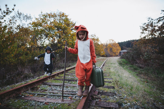 Kids dressed up like fox and raccoon walking on train tracks