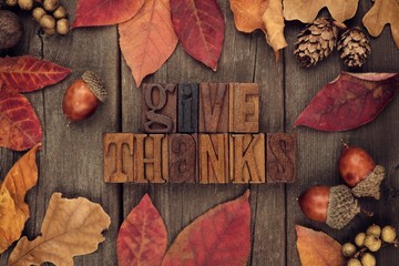 Give Thanks spelled with wooden letterpress with frame of autumn leaves over a rustic wood...