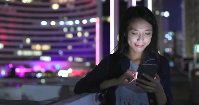 Woman sending sms on cellphone in city at night