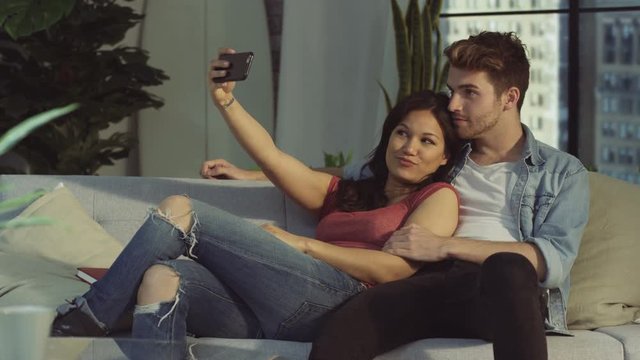  Affectionate couple relaxing at home & taking selfie with smartphone