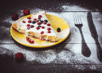 Homemade apple pie with white cream and berries sprinkled with powdered sugar on a yellow plate and a dark wooden background