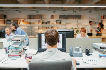 Back of businessman using headset facing coworkers rear view