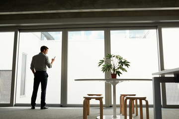 Silhouette of man looking at smartphone at window