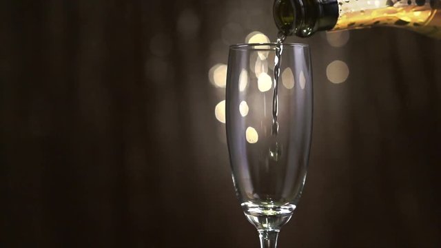 Champagne. Flute with sparkling wine. Pouring champagne over holiday golden blinking background closeup. Slow motion 4K UHD video 3840x2160
