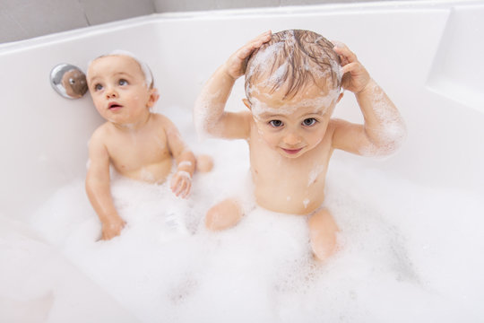 Two little boys having fun with water by taking bath in bathtub
