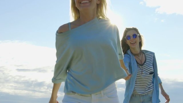 Two Beautiful Girls Holding Hands and Running into the Cloudless Happy Future. Clear Sky in the Background. Shot on RED EPIC-W 8K Helium Cinema Camera.