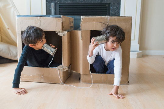 two children playing in boxes talking over a tin can telephone
