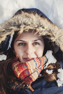 Woman with winter coat and fluffy hood lying down in snow