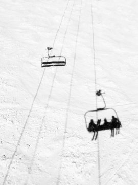 Shadow of three pople riding a chairlift on a groomed ski slope as an empty chair passes by