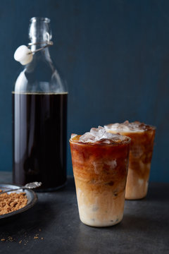 Iced lattes in glass with swirls shown with brown sugar and carafe of coffee