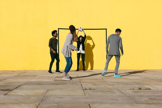 Group of friends having fun playing football in front of a yellow wall.