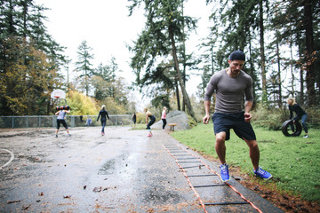Man doing agility ladder exercise at wet outdoor boot camp