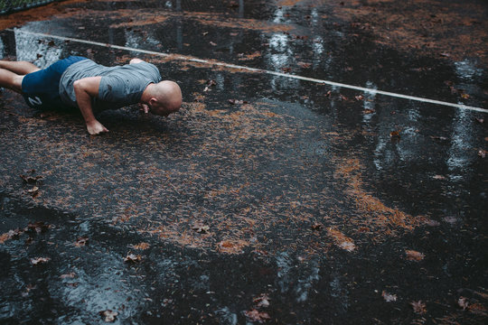 Man doing push-ups on fists on wet ground outside - Powered by Adobe