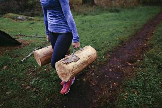 Woman walking with heavy logs at rainy outdoor bootcamp
