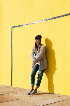 Young woman holding soccer ball in front of a yellow wall.