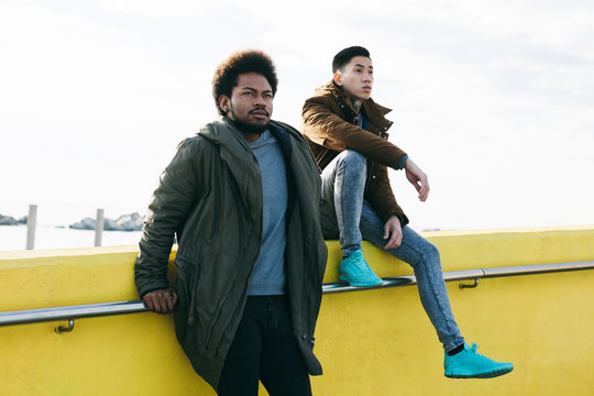 Two multicultural friends hanging out sitting on a wall.