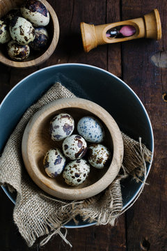 Quail eggs in bowls on a wooden background with an egg timer.