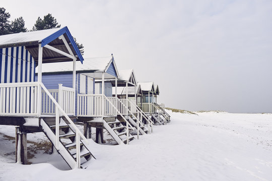 Beach huts covered in snow at low tide. Wells-next-the-sea, Norfolk, UK.