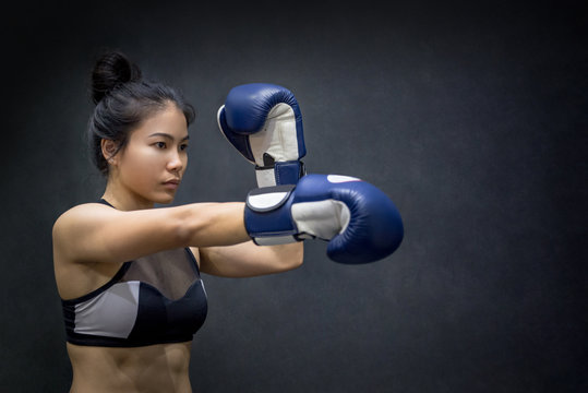 Beautiful young Asian woman posing with blue boxing gloves, black background