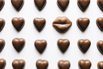 Close-up of lips and heart shaped chocolates on white background