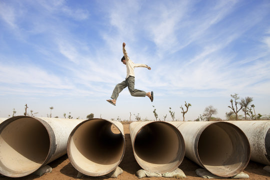 Boy jumping water pipes in desert, India
