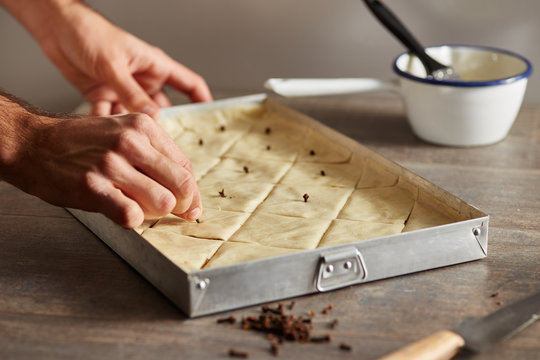 Man decorating cut uncooked baklava with cloves