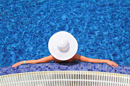 Woman in a white hat on the bllue pool background, relaxing in the water, shallow focus