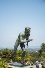 Fototapeta premium An antique sculpture of a man standing behind a background of blue sky and mid-ocean trees