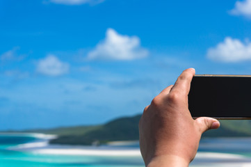 Tourist taking photo of tropical beach with his or her smartphone