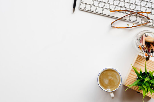 Stylish or designer minimalistic workplace with pc keyboard , brushes, office plant, glasses and coffee in flat lay style. White background. Top view.