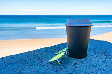 Coffee cup and sunglasses with beach on the background