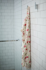 Floral nightgown hanging in white tiled bathroom