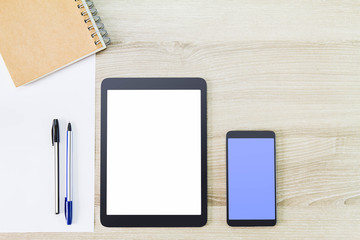 Blank white screen tablet computer with mobile phone, notebook, paper and pens on wooden desk