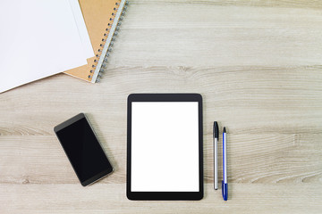 Blank white screen tablet computer with mobile phone, notebook, paper and pens on wooden desk