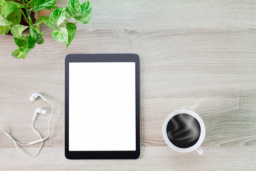 Blank white screen tablet computer with hot coffee cup, earphone and green plant pot on wooden desk