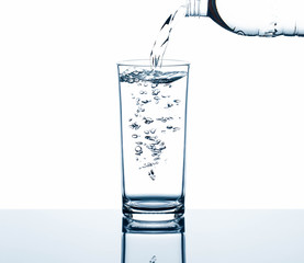 Drinking water pouring from bottle into glass with air bubbles with reflection on glass table isolated on white background