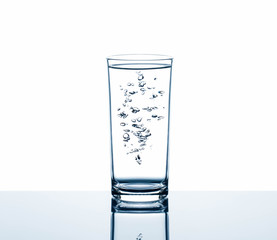 Drinking water in glass with air bubbles on reflection glass table isolated on white background