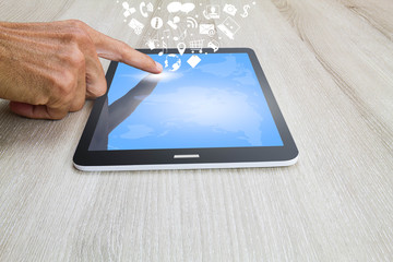 Man's hand touching on tablet computer with world map, social and business icons on wooden desk, business technology concept